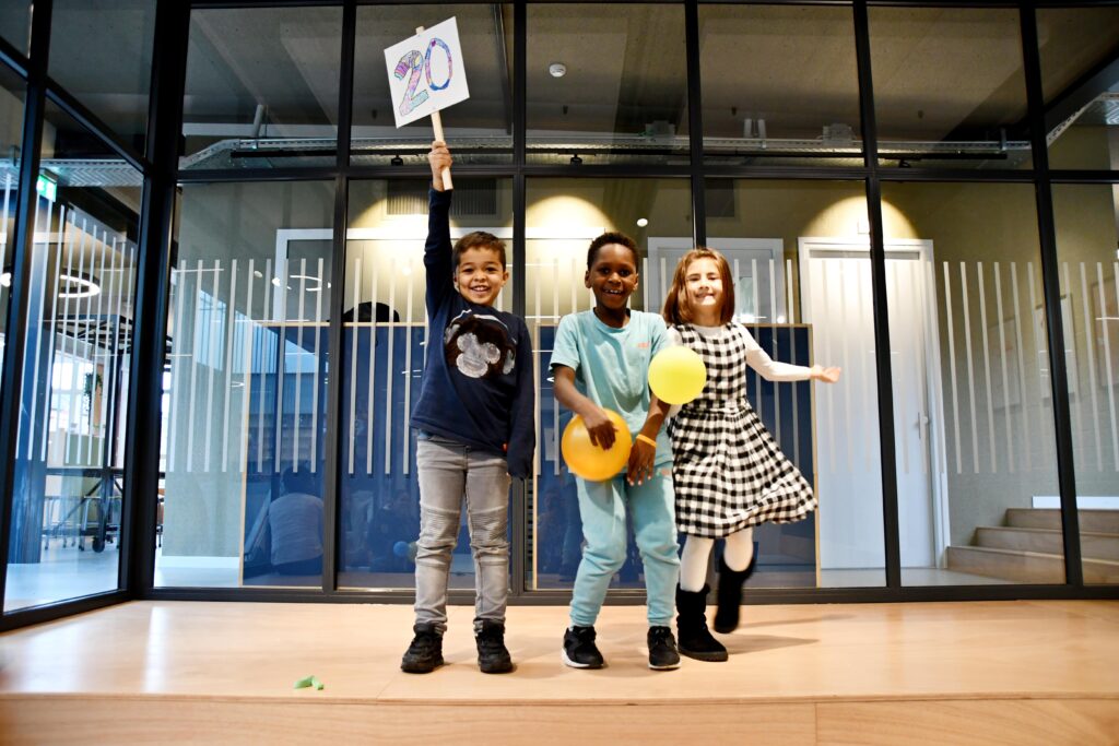 drie kinderen poseren feestelijk met balonnen en een bord