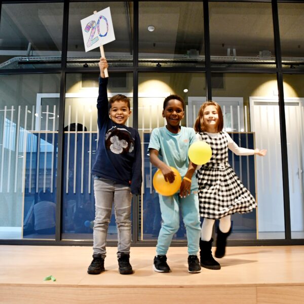 drie kinderen poseren feestelijk met balonnen en een bord